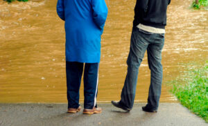 Two people with their backs to a flooded roadway.